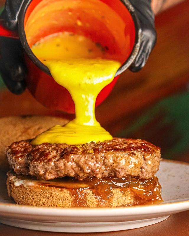 Cheddar sendo despejado sobre um hambúrguer